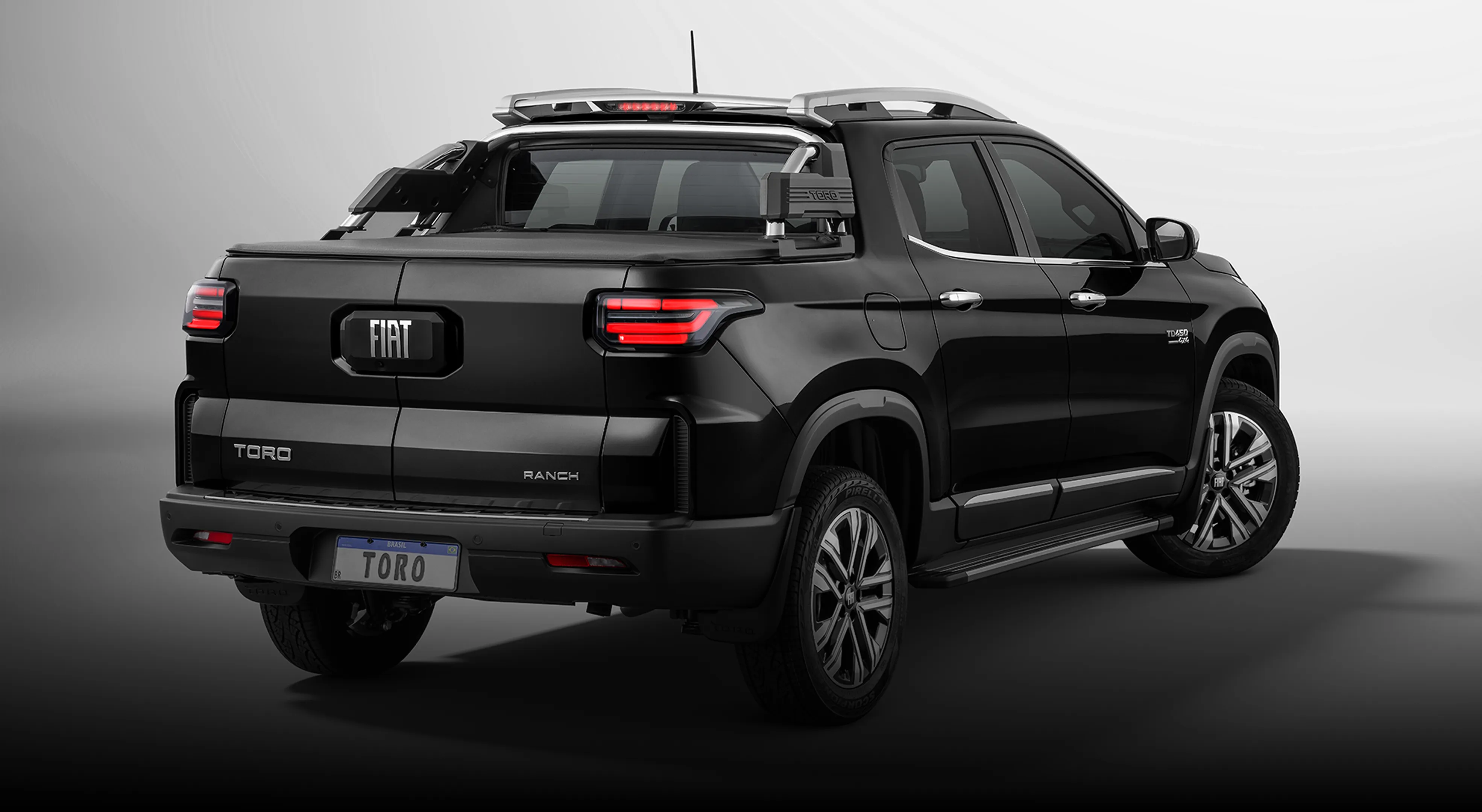 Lateral traseira da Fiat Toro Ranch preta com lanternas acesas, rodas de liga-leve, estribo lateral e placa Toro.