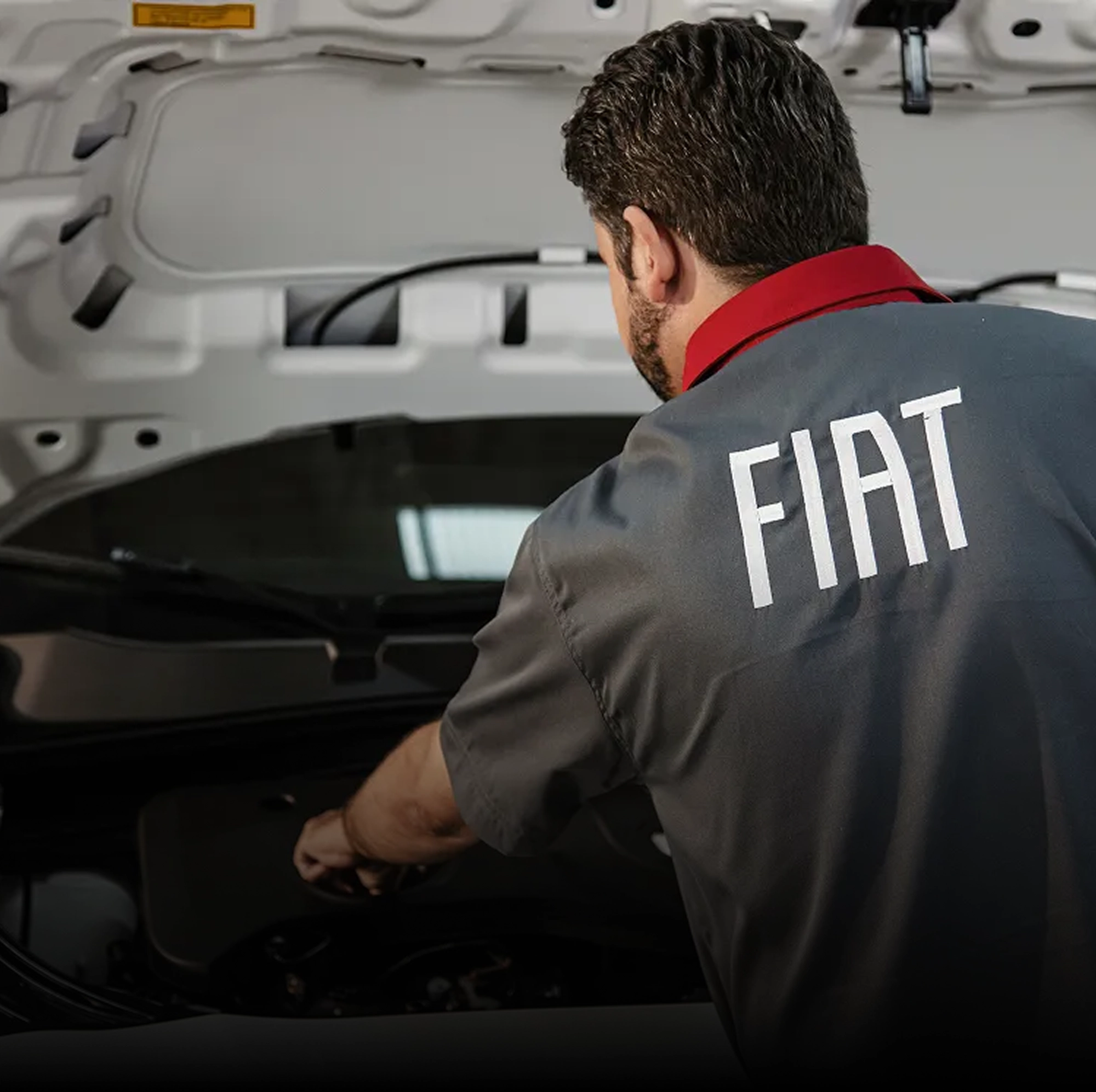Pessoa vestindo uniforme com logotipo Fiat trabalha no compartimento do motor da Fiat Toro com capô aberto.
